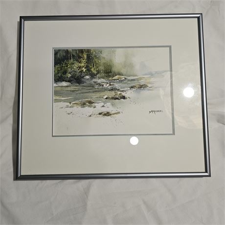 Framed watercolor print likely depicting a rocky stream or shoreline scene