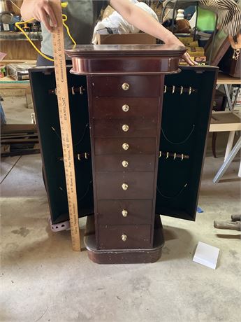 Wooden jewelry armoire with multiple drawers and side cabinets for storage.