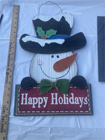 rustic wooden snowman sign that says "Happy Holidays." It is a holiday-themed wa