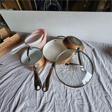 two copper-colored pots with lids, a frying pan, and a colander or strainer.